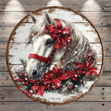 A white horse adorned with a red bow and surrounded by red poinsettia flowers and pine branches, set against a snowy background.