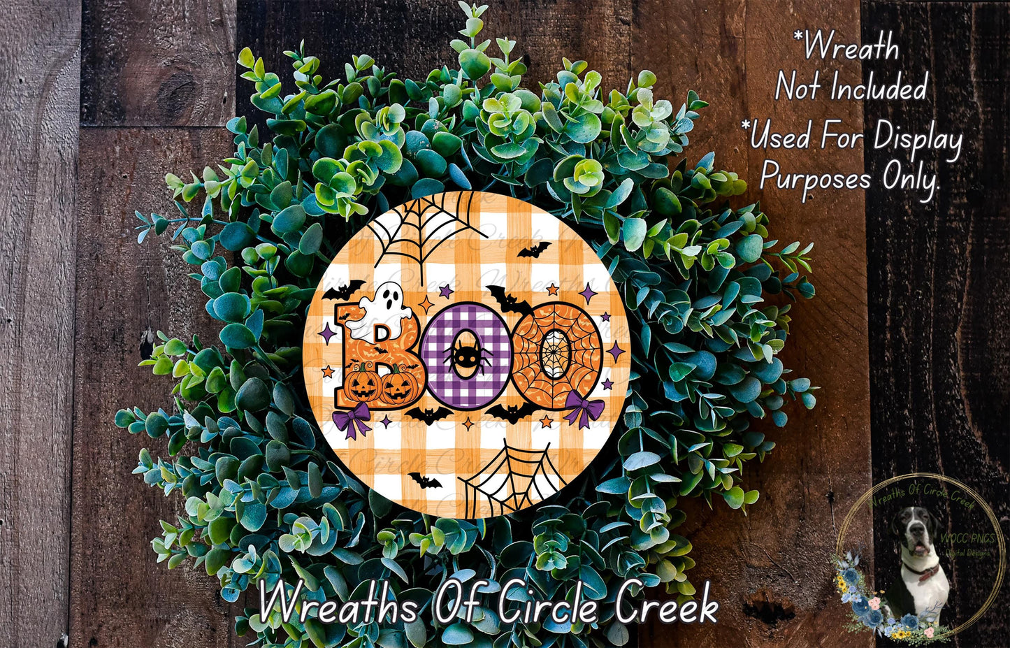 a Halloween-themed wreath made of green foliage and decorated with the word "Boo" in a checkered pattern. The wreath is displayed on a wooden surface, and there is a small dog visible in the background.