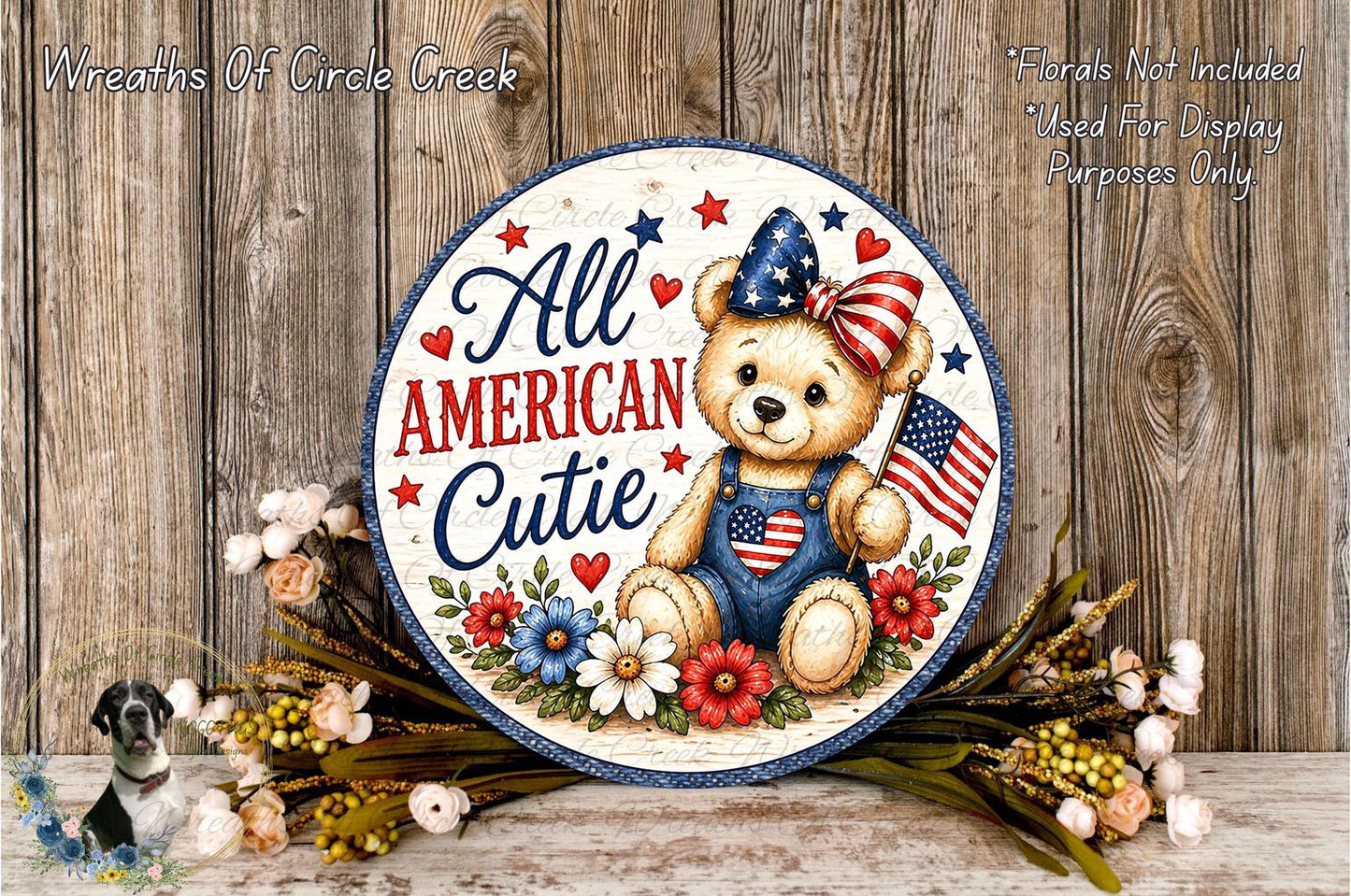 A decorative sign featuring a teddy bear wearing patriotic attire, surrounded by flowers and a patriotic flag, with the text "All American Cutie" on it.