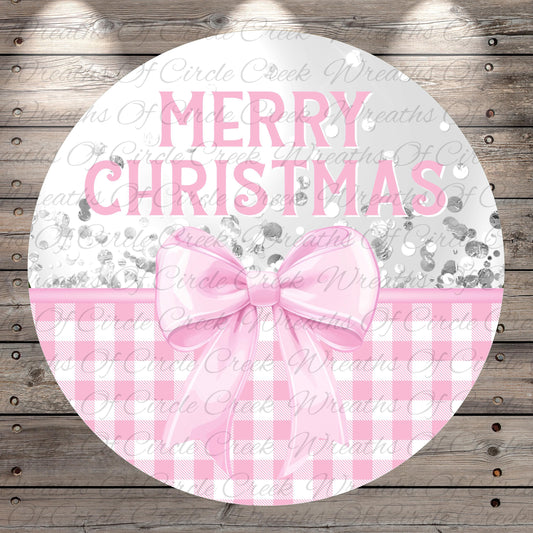 A circular sign with the text "Merry Christmas" in pink letters, surrounded by a pink bow and a gingham pattern.