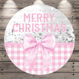 A circular sign with the text "Merry Christmas" in pink letters, surrounded by a pink bow and a gingham pattern.