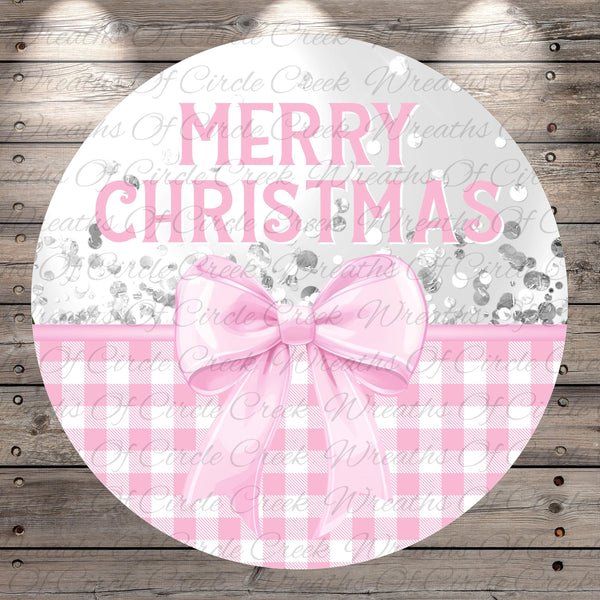 A circular sign with the text "Merry Christmas" in pink letters, surrounded by a pink bow and a gingham pattern.