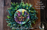 a wreath with a colorful mask at its center, surrounded by a lush green plant arrangement.