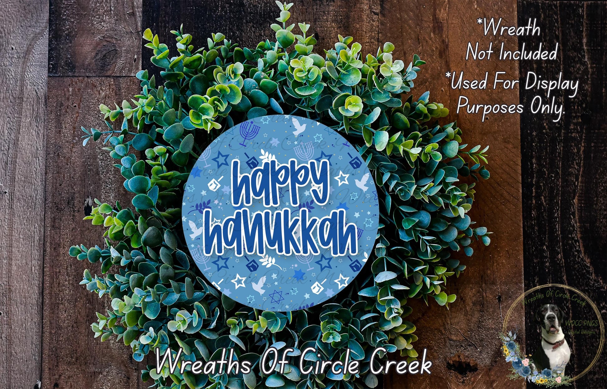 A wreath made of green leaves and flowers, with a blue circular sign that says "Happy Hanukkah" in the center.