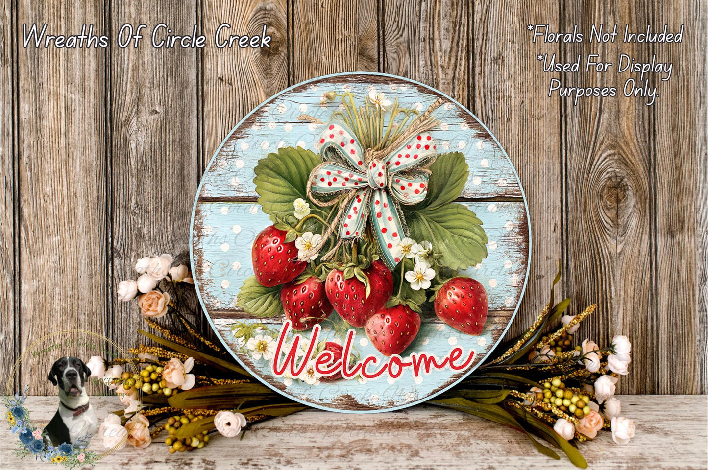 A round wooden sign with a bow of red and white, displaying a bunch of red strawberries and green leaves, surrounded by flowers and greenery. The sign has the word "Welcome" written on it.