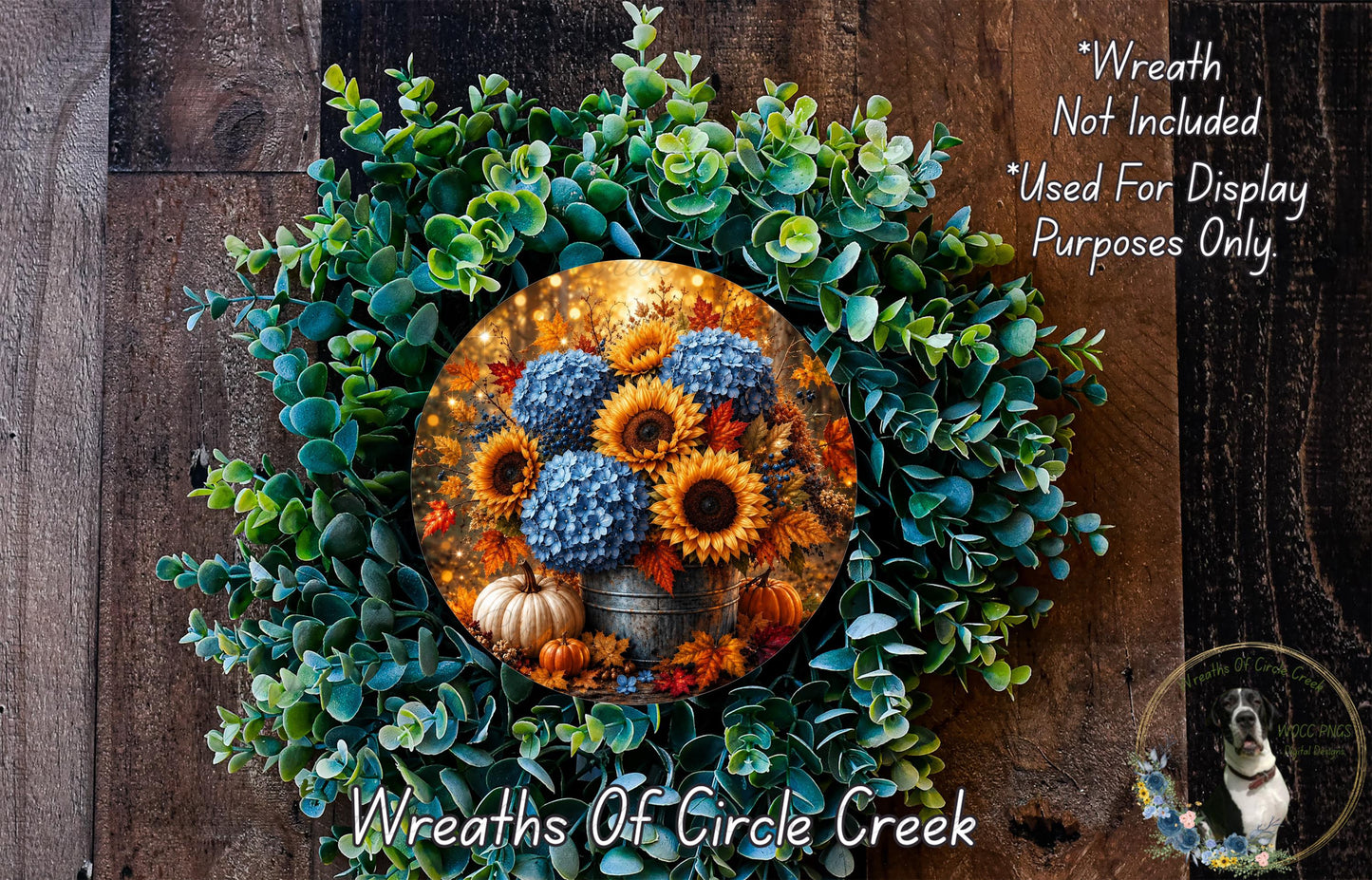 a wreath made of various plants, including sunflowers and greenery, with a circular arrangement of flowers in the center. The wreath is displayed on a wooden surface, and there is a small dog visible in the bottom right corner of the image.