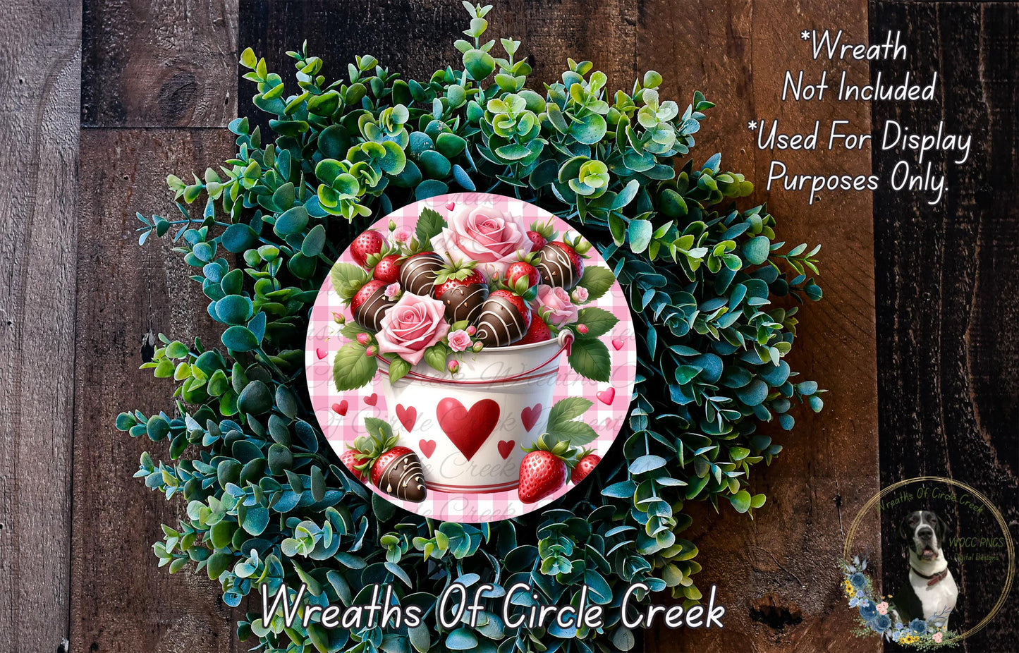 A wreath made of green foliage and pink roses, with a white vase containing strawberries and a heart-shaped decoration.