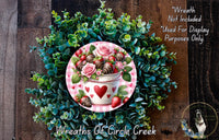 A wreath made of green foliage and pink roses, with a white vase containing strawberries and a heart-shaped decoration.