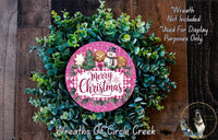 A Christmas wreath made of evergreen branches and a pink circular sign with the text "Merry Christmas" and a snowman decoration.