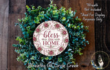 A wreath made of various green and brown foliage, with a circular sign in the center that reads "bless this home".