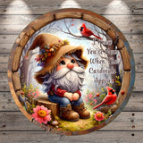 A gnome wearing a straw hat and holding a flower sits on a tree stump in a forest, with two red birds nearby.