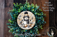 A wreath made of green foliage and featuring a snowman as the central decorative element.