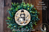 A wreath made of green foliage and featuring a snowman as the central decorative element.