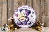 A round decorative plate with a teddy bear holding an envelope, surrounded by flowers and a wooden background.