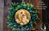A wreath with a circular arrangement of greenery and a depiction of the Holy Family, including Jesus, Mary, and Joseph, surrounded by flowers.