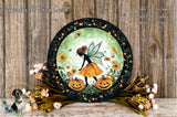 A decorative plate featuring a fairy with wings and a pumpkin, surrounded by flowers and a wooden background.