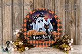 a Halloween-themed wreath with a ghost, a cat, and pumpkins, along with a banner that says "Boo Y'all". The wreath is displayed on a wooden surface, surrounded by flowers and greenery.