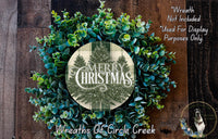 a Christmas wreath made of various green plants, including eucalyptus and other foliage, arranged around a circular design with the text "Merry Christmas" and "Wreaths of Circle Creek".