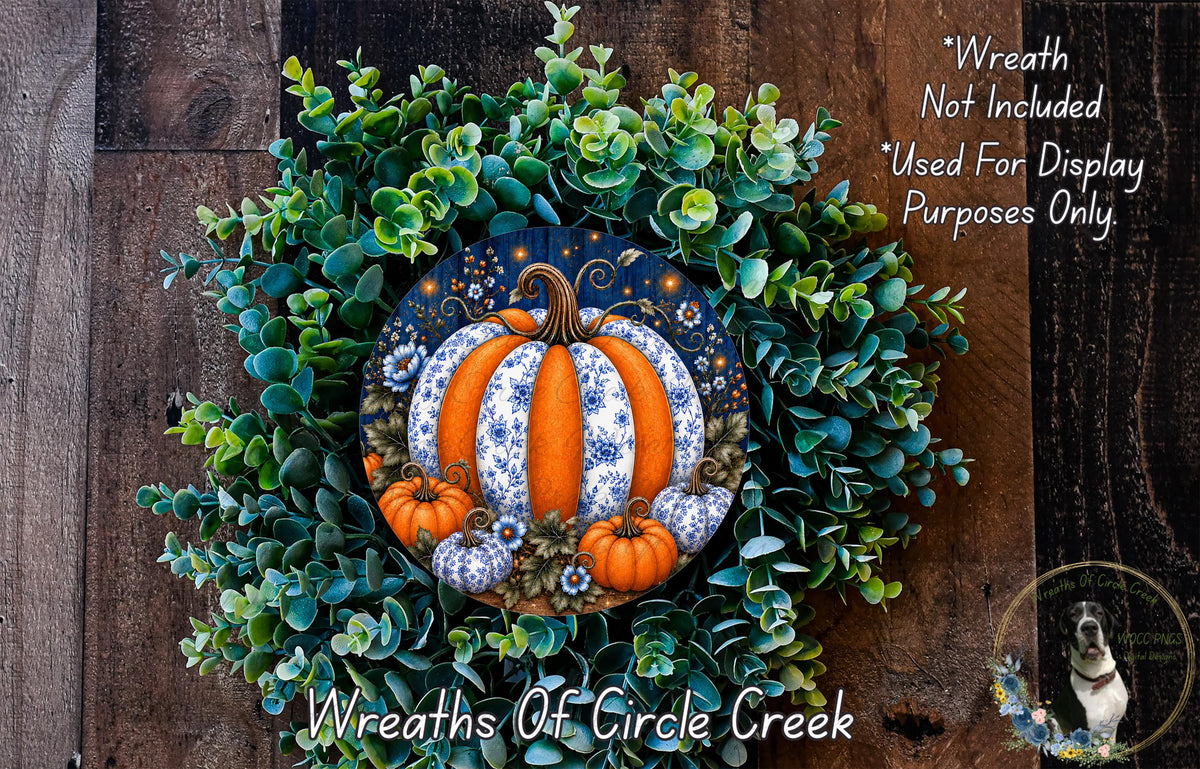 A wreath made of green leaves and orange pumpkins, with a large white and blue pumpkin at the center. The wreath is displayed on a wooden surface.