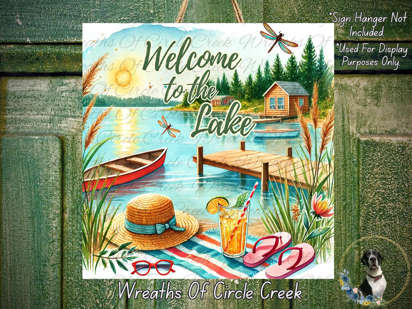The image is a vibrant and colorful illustration of a lakeside scene, featuring a wooden cabin, a dock, a boat, a straw hat, sunglasses, and a drink. The text "Welcome to the Lake" is prominently displayed, along with the phrase "Wreaths of Circle Creek".