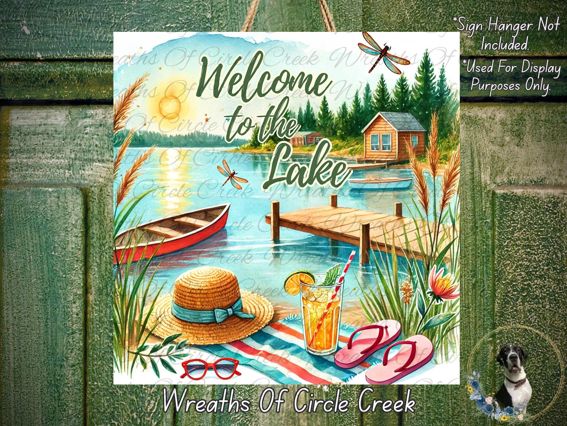The image is a vibrant and colorful illustration of a lakeside scene, featuring a wooden cabin, a dock, a boat, a straw hat, sunglasses, and a drink. The text "Welcome to the Lake" is prominently displayed, along with the phrase "Wreaths of Circle Creek".