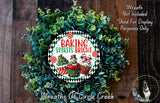 a wreath made of green leaves and decorated with a sign that reads "Baking Spices Bright". The wreath is placed on a wooden surface, and there is a small dog visible in the bottom right corner of the image.