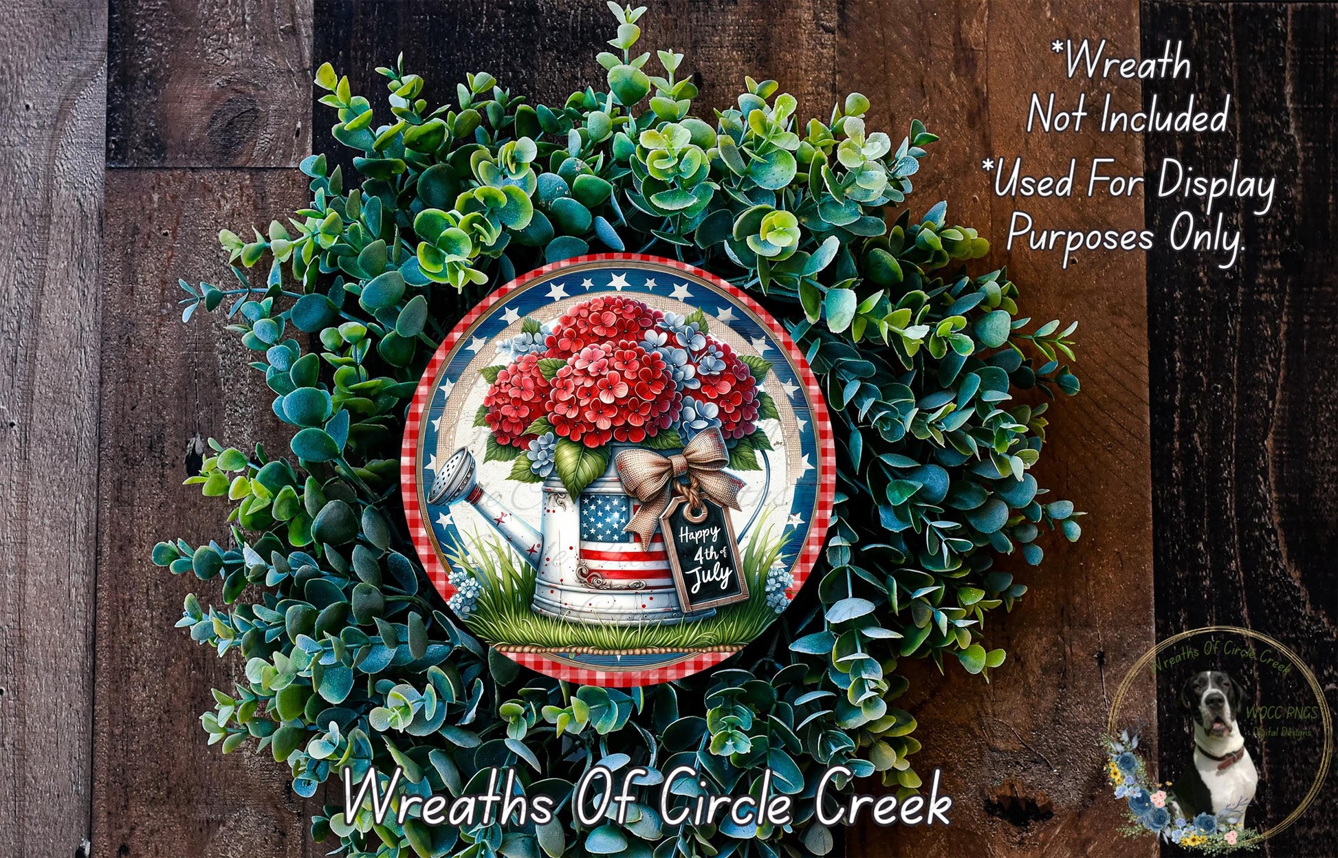 a wreath made of green foliage and red flowers, with a patriotic design that includes an American flag and a patriotic ribbon. The wreath is displayed on a wooden surface, and there is a small dog in the bottom right corner of the image.