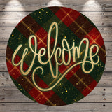 A circular sign with the word "Welcome" written in cursive script against a background of a plaid pattern in red, green, and gold colors.