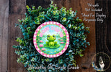 a wreath with a frog on it, surrounded by greenery. The wreath is placed on a wooden surface, and there is a text overlay that reads "Welcome to our pond" and "Wreaths of Circle Creek".