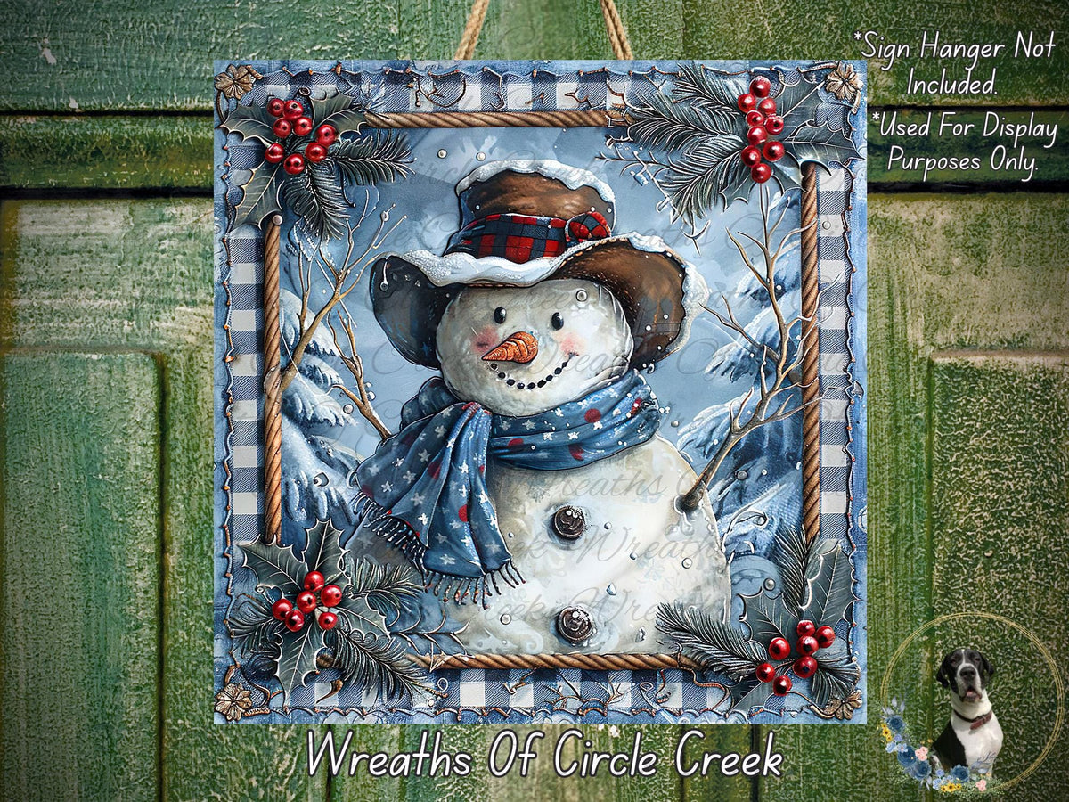 A snowman wearing a blue scarf and hat, surrounded by red berries and holly leaves, is displayed in a decorative frame against a snowy background.