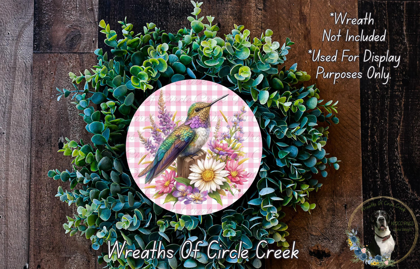 A wreath made of green foliage and flowers, with a bird perched on a flower, is displayed on a wooden surface.