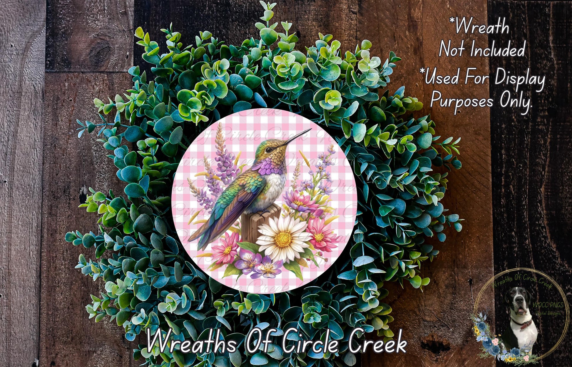 A wreath made of green foliage and flowers, with a bird perched on a flower, is displayed on a wooden surface.