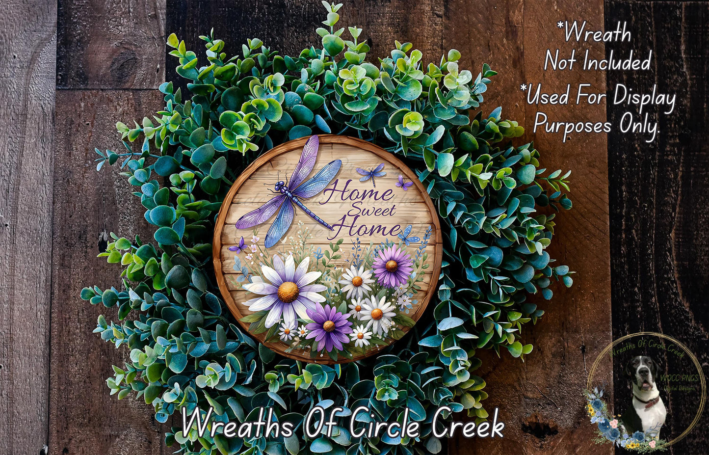 a wreath made of various green plants and flowers, with a wooden sign that reads "Home Sweet Home" in the center. The wreath is displayed on a wooden wall, and there is a small dog in the bottom right corner of the image.