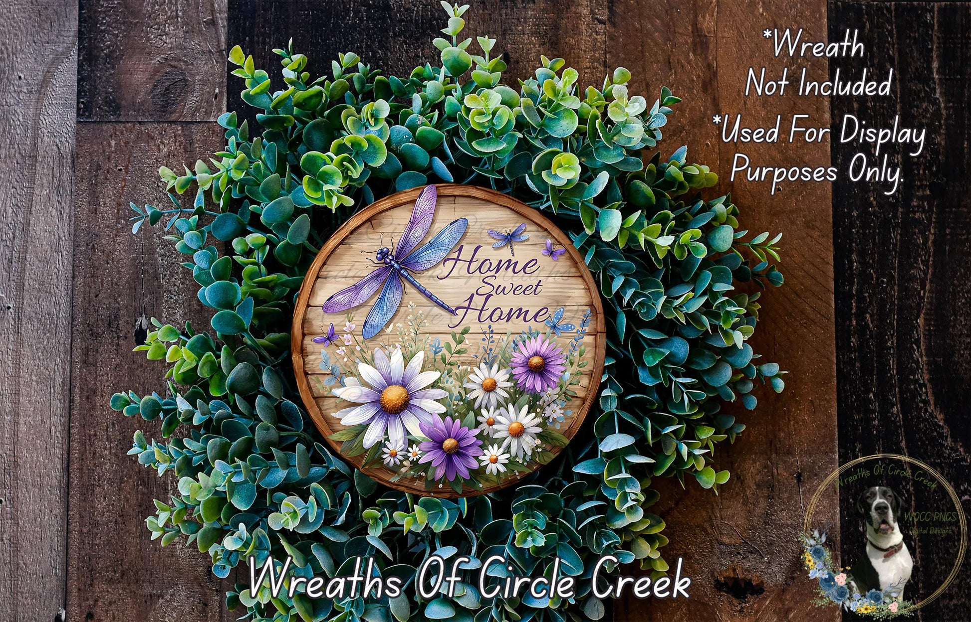 a wreath made of various green plants and flowers, with a wooden sign that reads "Home Sweet Home" in the center. The wreath is displayed on a wooden wall, and there is a small dog in the bottom right corner of the image.