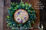a wreath made of various green plants and flowers, with a wooden sign that reads "Home Sweet Home" in the center. The wreath is displayed on a wooden wall, and there is a small dog in the bottom right corner of the image.