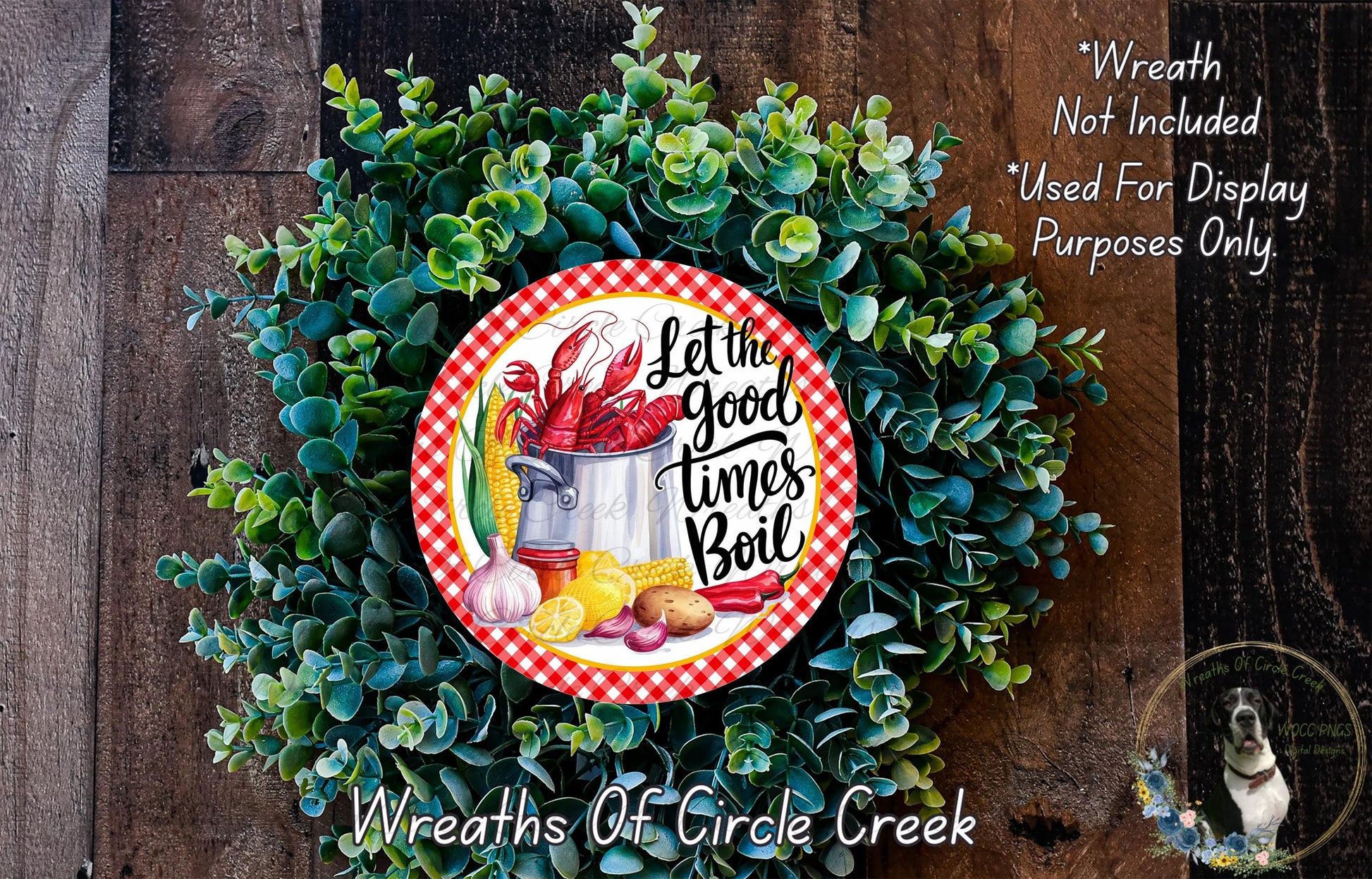 A wreath made of green foliage and featuring a red and white checkered border, with a circular design in the center displaying the text "Let the good times boil" surrounded by various food items such as a lobster, corn, and potatoes.