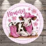 A cow wearing a pink cowboy hat and boots, with a pink bandana around its neck, is sitting on a grassy area with pink flowers in the background.