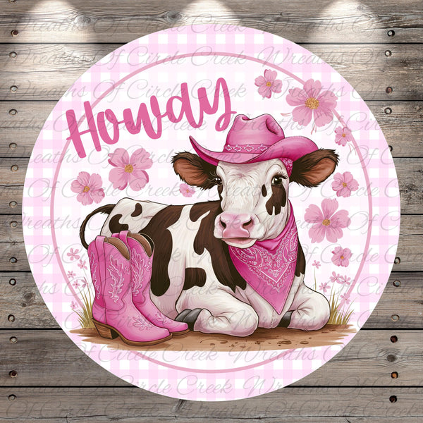 A cow wearing a pink cowboy hat and boots, with a pink bandana around its neck, is sitting on a grassy area with pink flowers in the background.