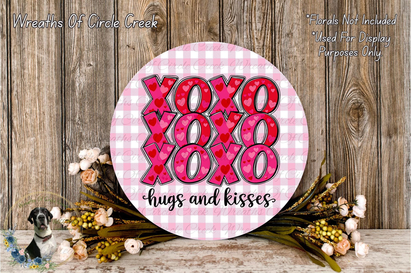 a round sign with the text "XOXO XOXO XOXO hugs and kisses" written on it, surrounded by a floral arrangement and a wooden background.