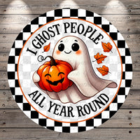 A round sign with a cartoon ghost holding a pumpkin and the text "I ghost people all year round" on a checkered background.