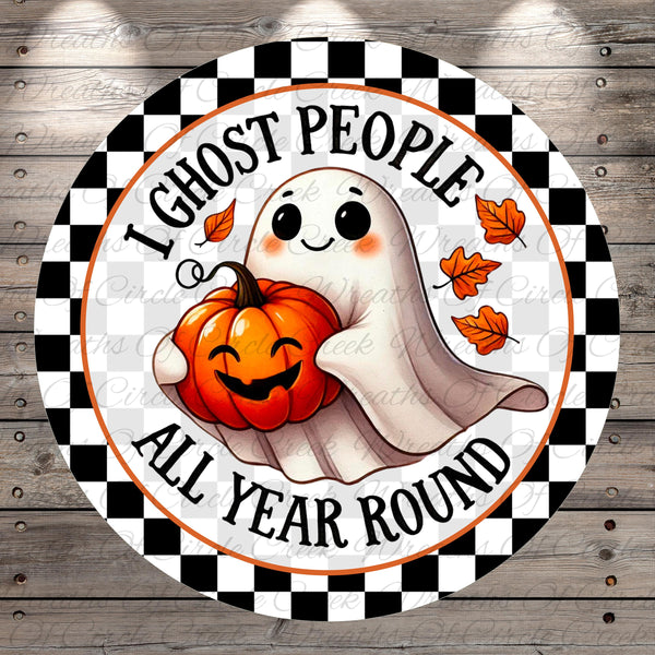 A round sign with a cartoon ghost holding a pumpkin and the text "I ghost people all year round" on a checkered background.