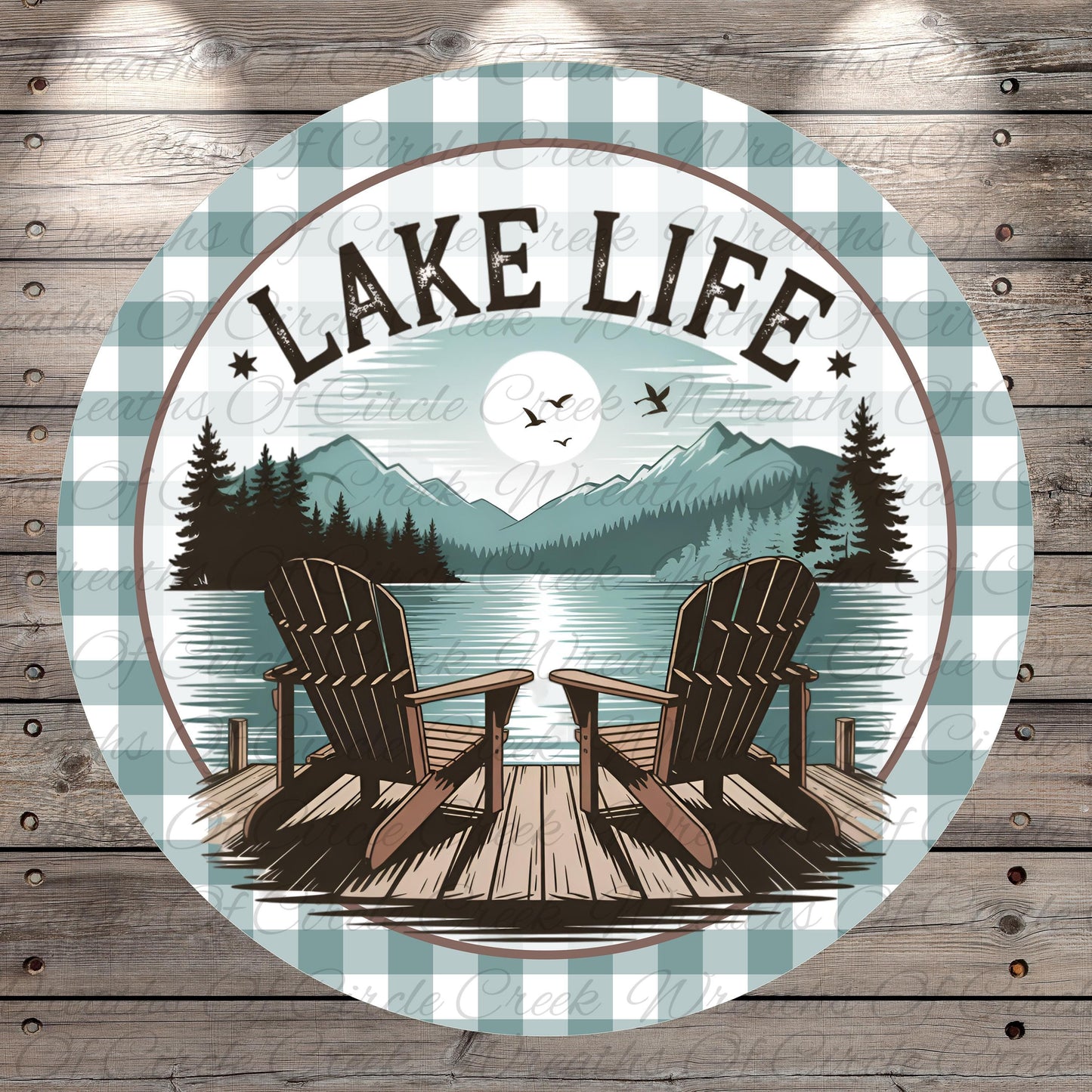A circular design featuring a lake with a wooden dock and two Adirondack chairs, surrounded by mountains and pine trees. The text "LAKELIFE" is prominently displayed above the chairs.