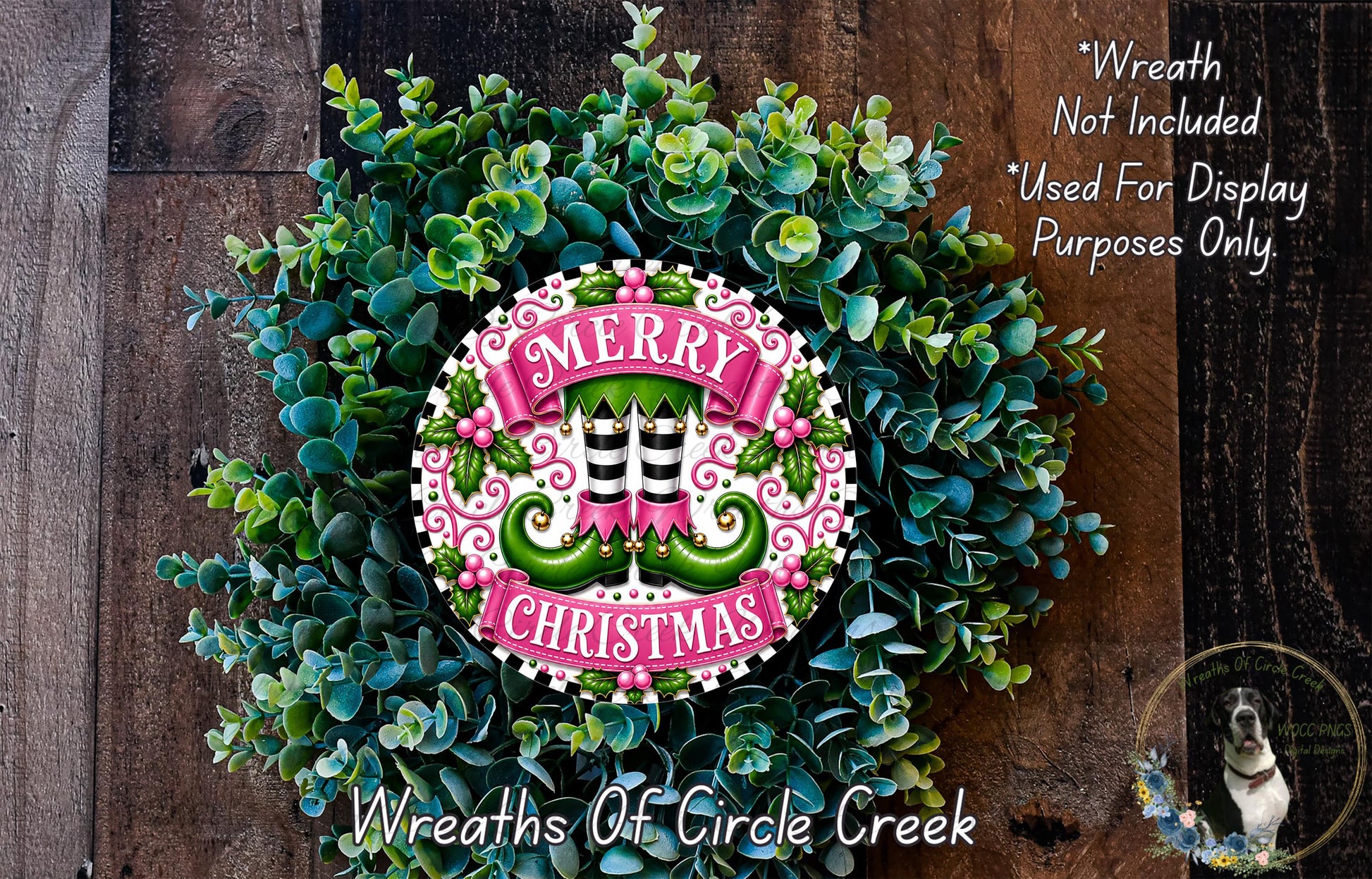 A wreath made of green leaves and flowers, with a pink and white circular sign that says "MERRY CHRISTMAS" in the center. The wreath is displayed on a wooden surface, and there is a text overlay that says "Wreath Not Included * Used For Display Purposes Only".