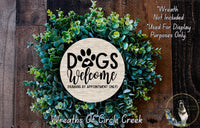a wreath made of green leaves and a circular sign that says "Dogs Welcome" in bold black letters.