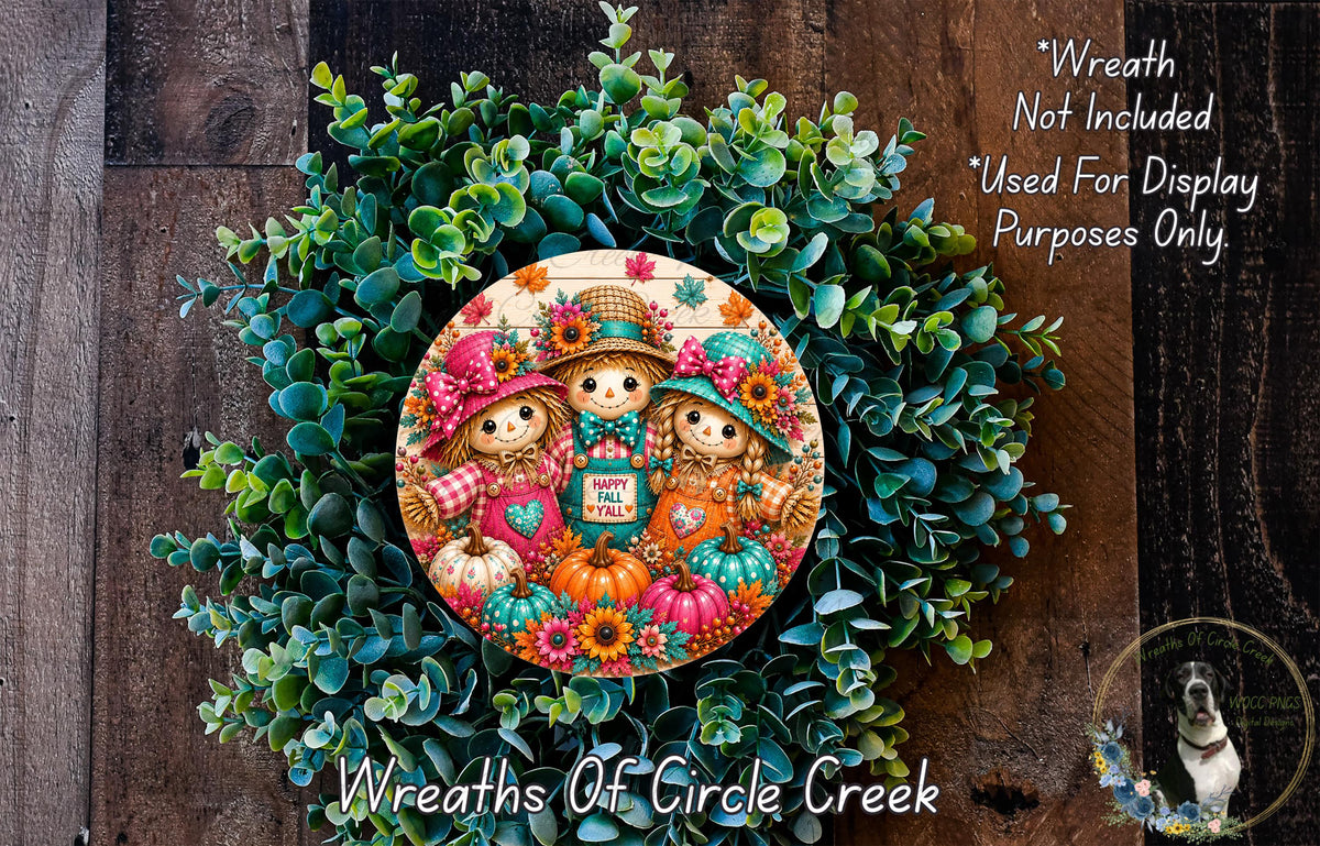 a wreath with a decorative design of three scarecrow characters, surrounded by a lush green plant. The wreath is placed on a wooden surface, and there is a small dog visible in the bottom right corner of the image.