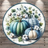 A circular arrangement of three pumpkins, each with a distinct pattern, surrounded by cotton bolls and leaves, set against a wooden background.