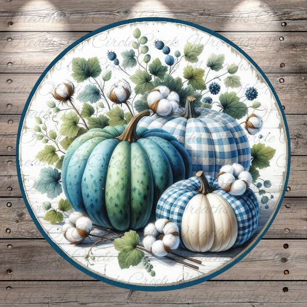 A circular arrangement of three pumpkins, each with a distinct pattern, surrounded by cotton bolls and leaves, set against a wooden background.