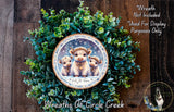 A wreath made of green leaves and flowers, with a circular ornament featuring three cows and the text "Let it snow" on it.