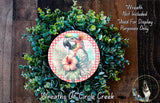 A wreath made of green leaves and a red and white checkered plate featuring a colorful parrot and a pink hibiscus flower.
