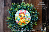 a wreath with a cartoon duck wearing a pink bow, surrounded by green foliage and decorated with Easter eggs.